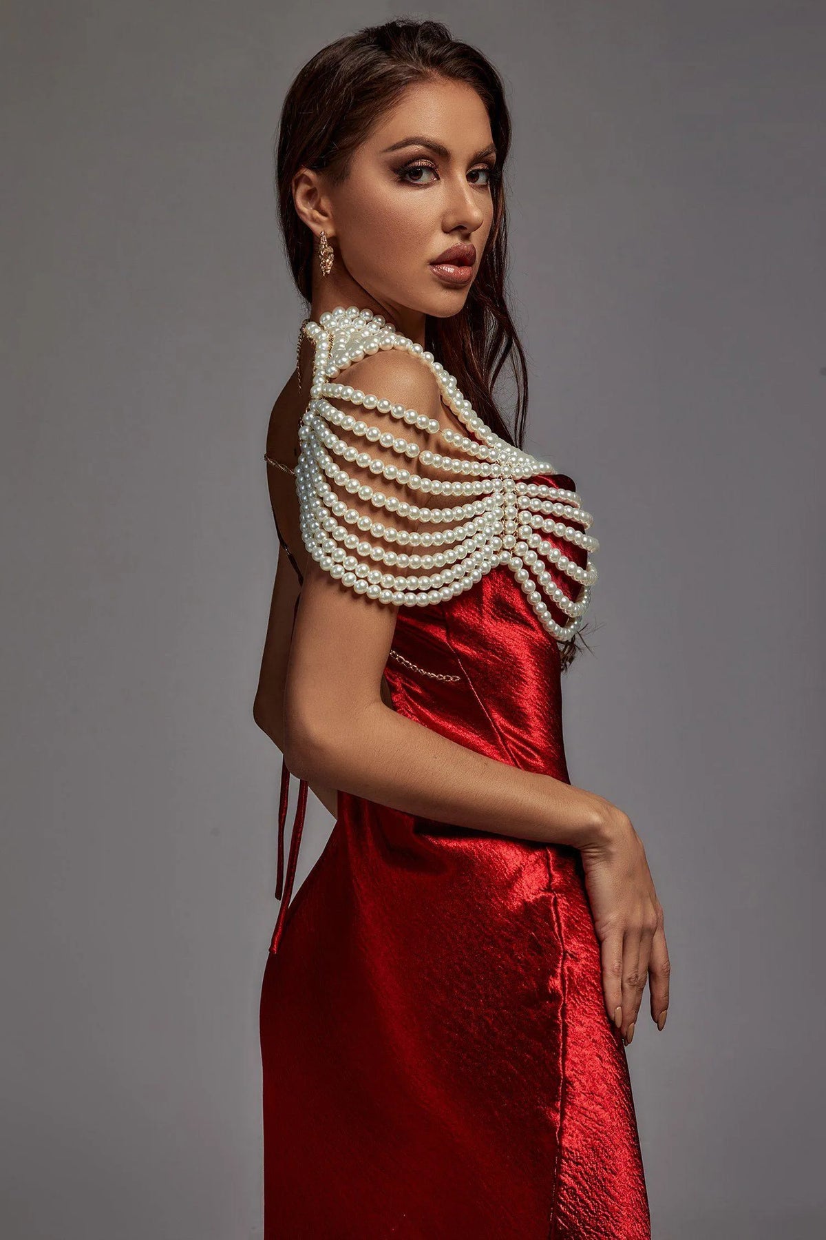 Woman wearing a red dress with pearl shoulder embellishments against a gray background